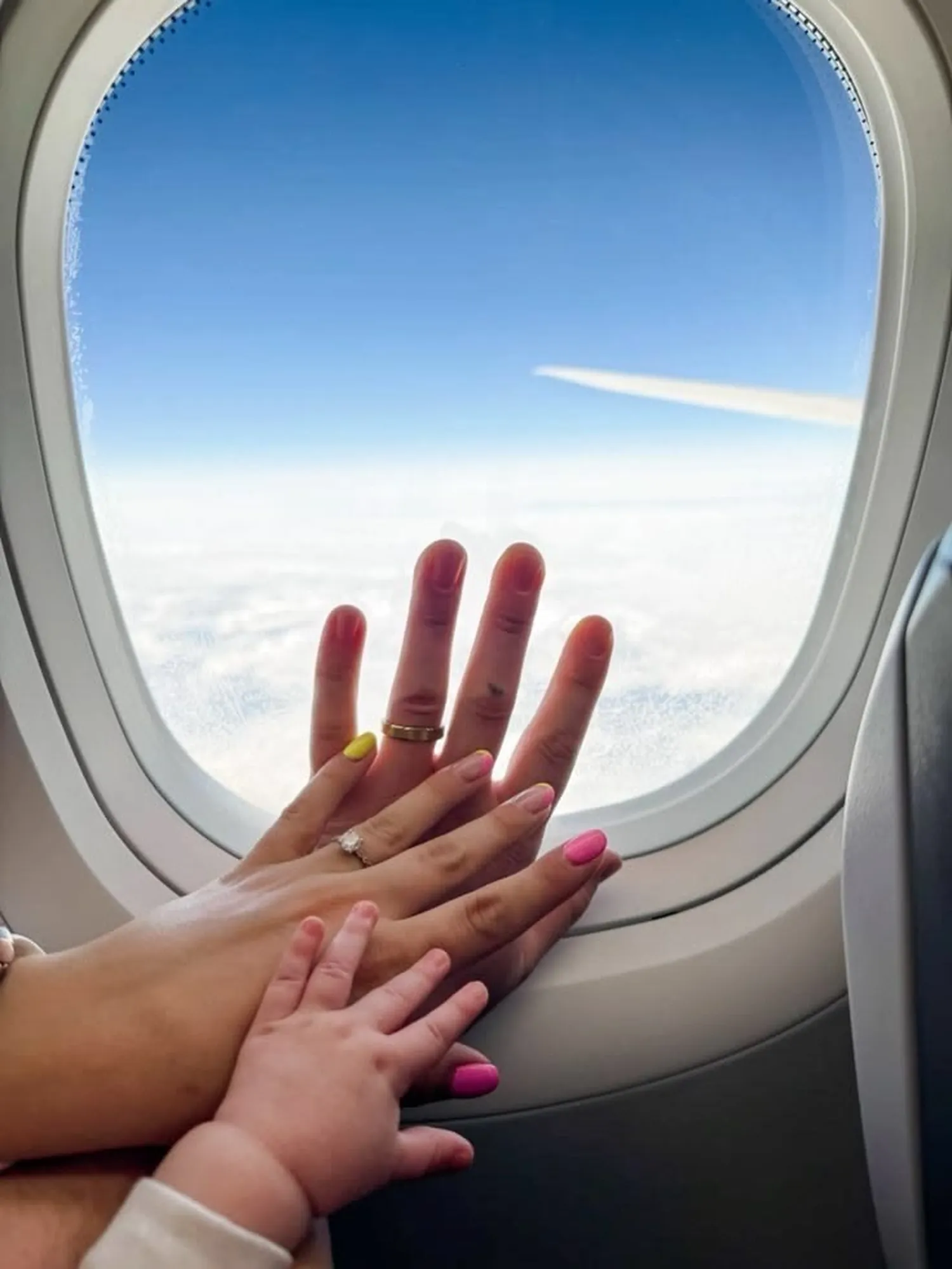 Mani di mamma e bambino sul finestrino dell'aereo, tra le nuvole